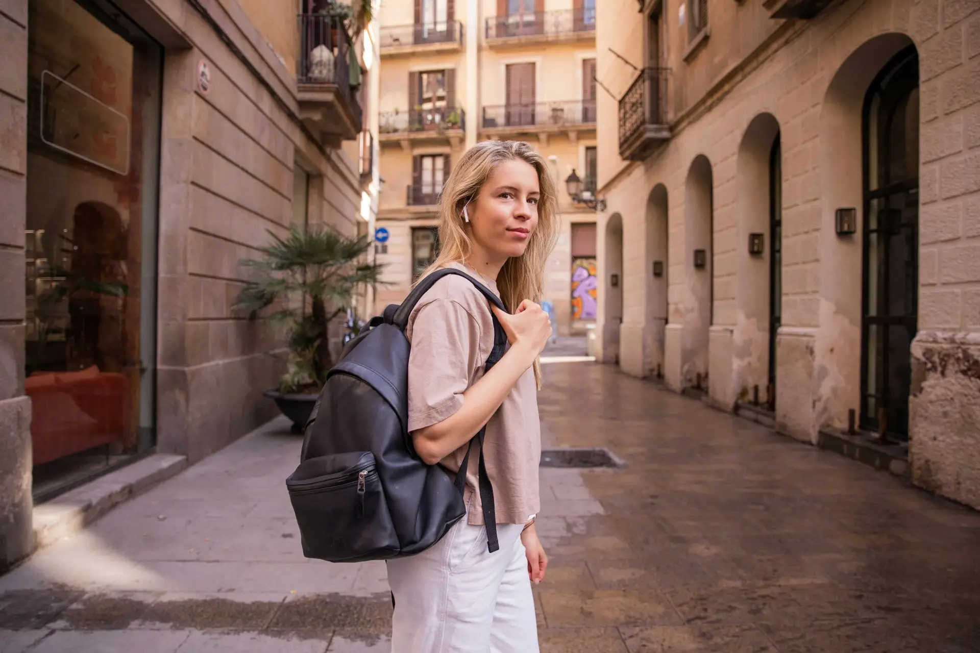 Young expat traveler with backpack walking through a sunny Spanish street, representing travel insurance from Spain